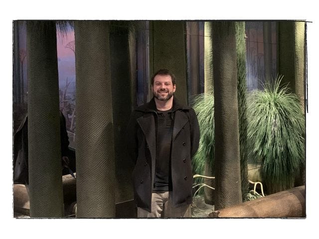 A handsome gentleman stands smiling at the photographer.