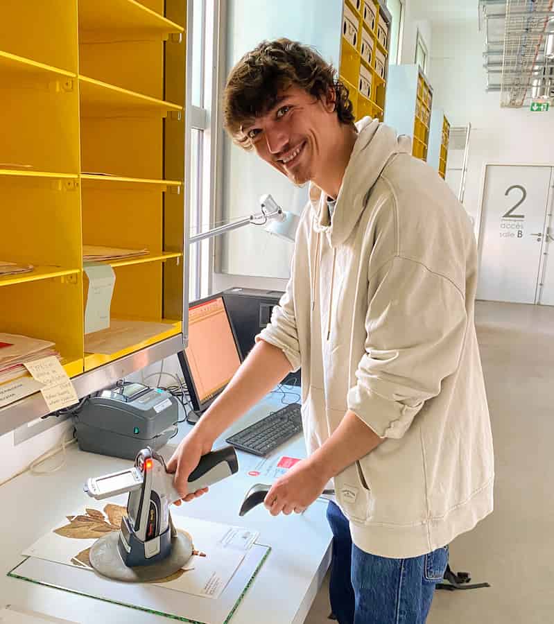 A handsome young man appearing to zap a herbarium specimen with what looks like a cross between a tricorder and a phaser pistol.