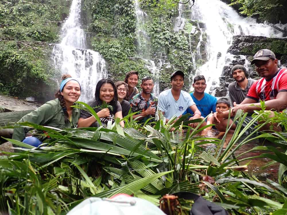 A team of young researchers smile at the camera in front of a tropical waterfall.