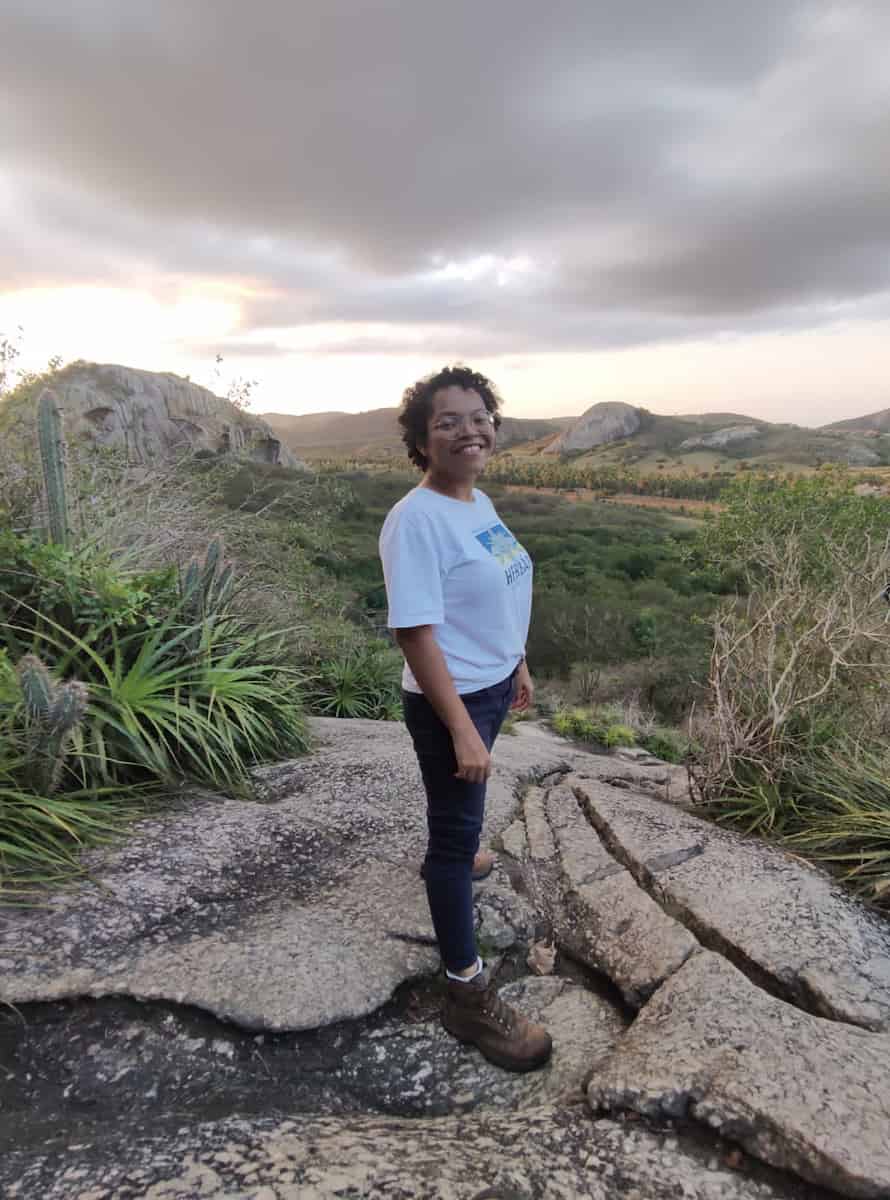 A woman stands side-on in the wild smiling at the camera.