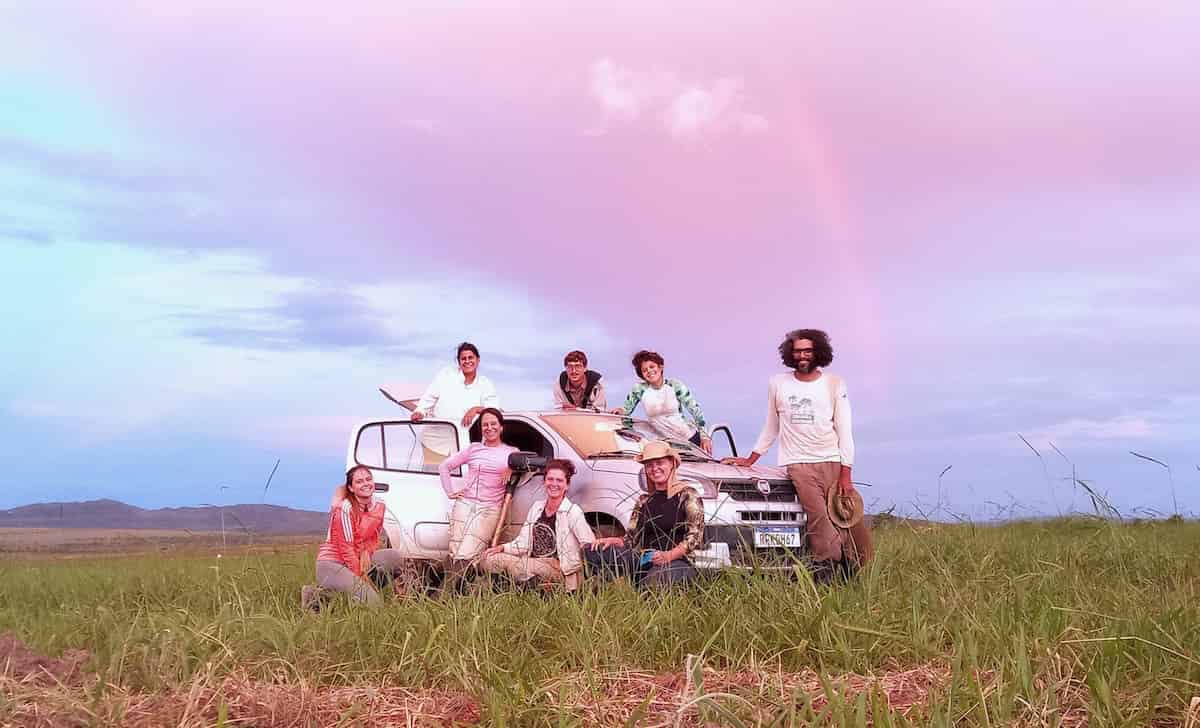 A group of scientists in a grassland under a surprisingly pink sky.
