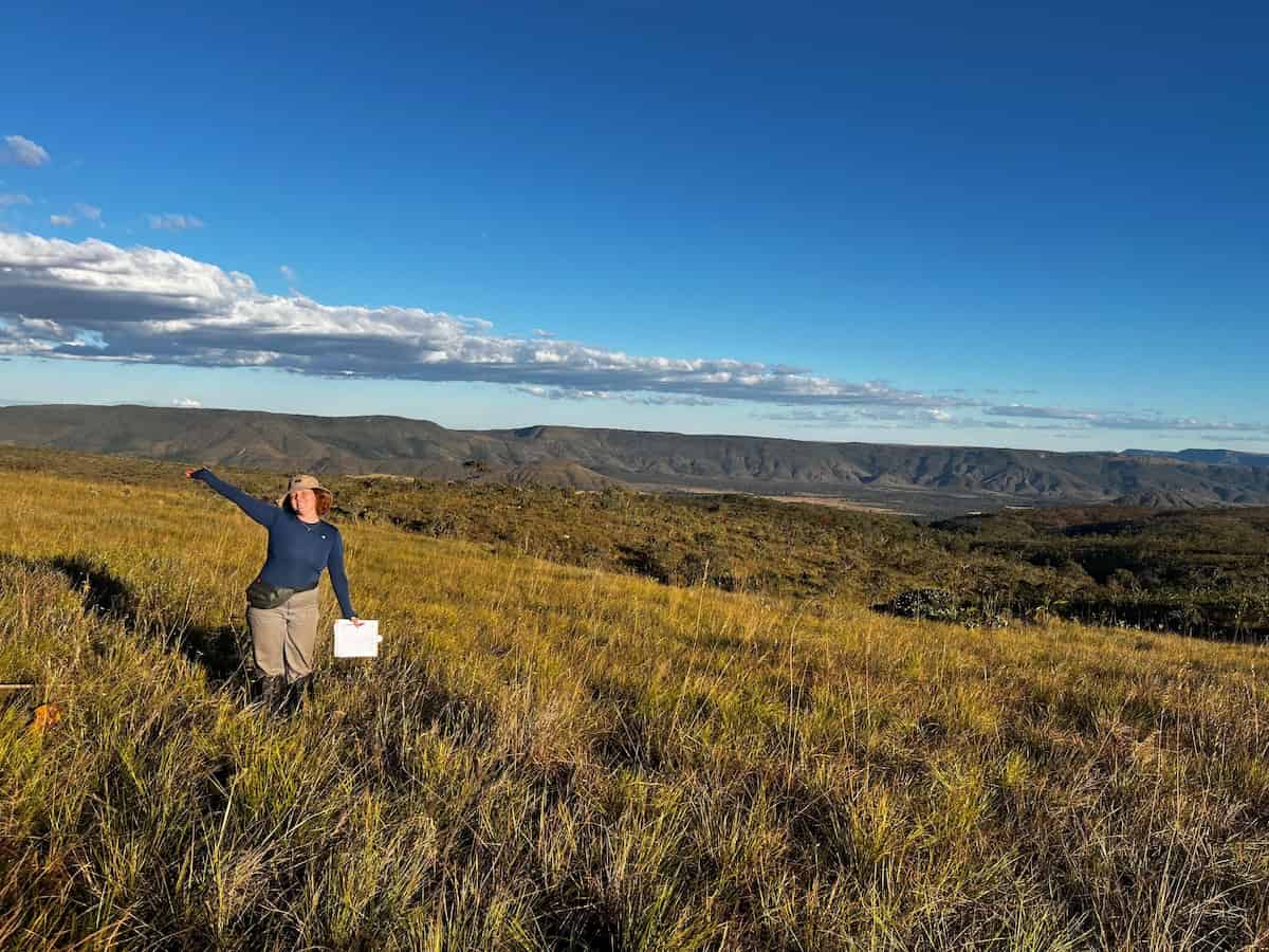 A woman smiling to the camera in a wide open grassland.