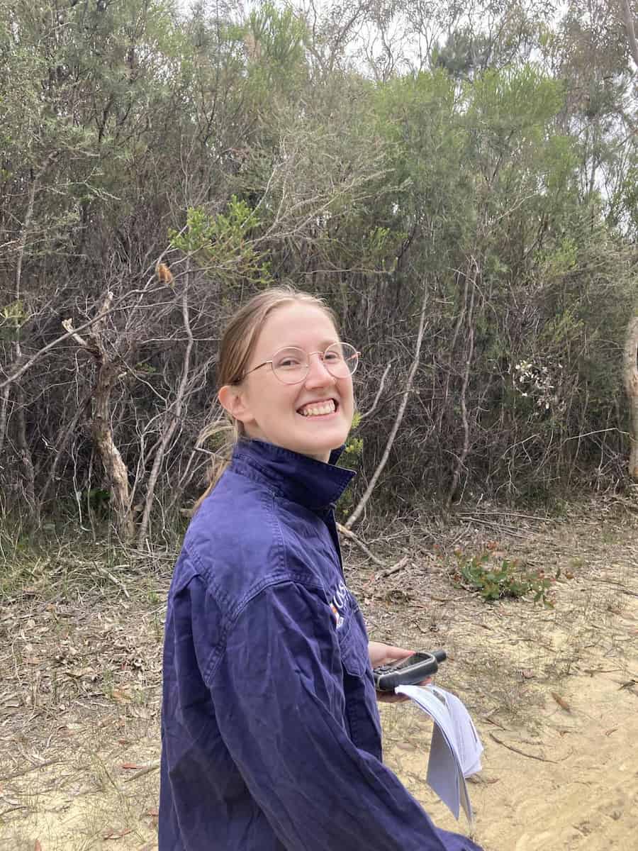 A woman standing in scrubland, smiling.