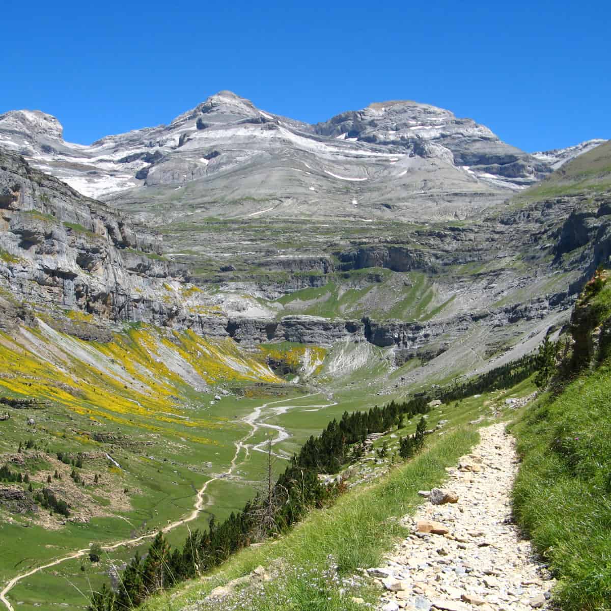 A hiking trail winds along a steep slope looking towards the Monte Perdido massif in the Pyrenees.