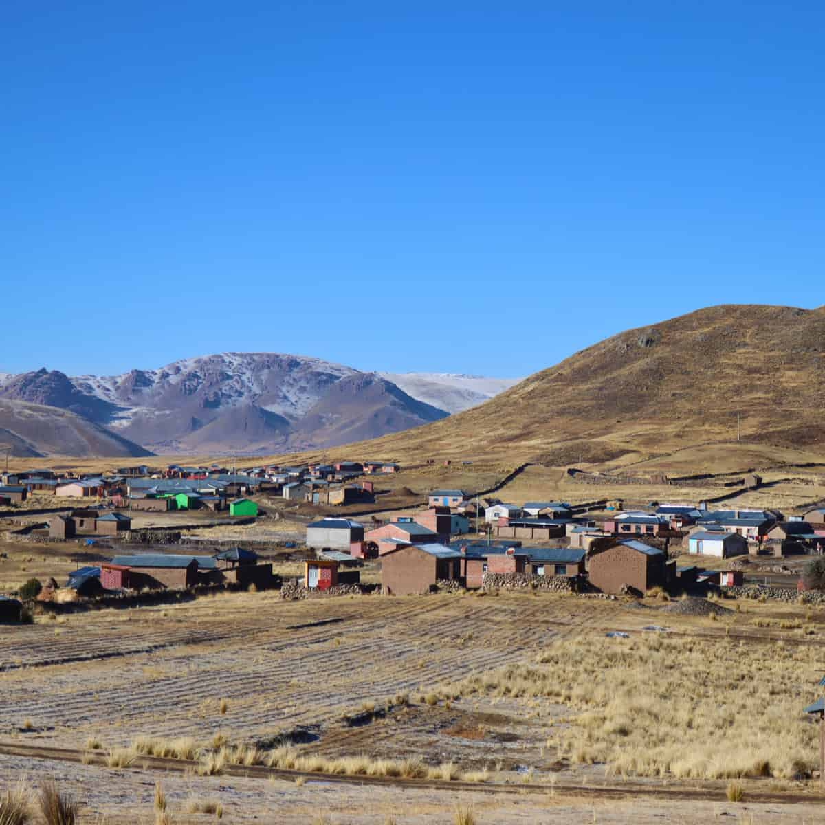 View of a contemporary Andean village with colourful houses scattered across high-altitude grassland, with snow-capped mounta