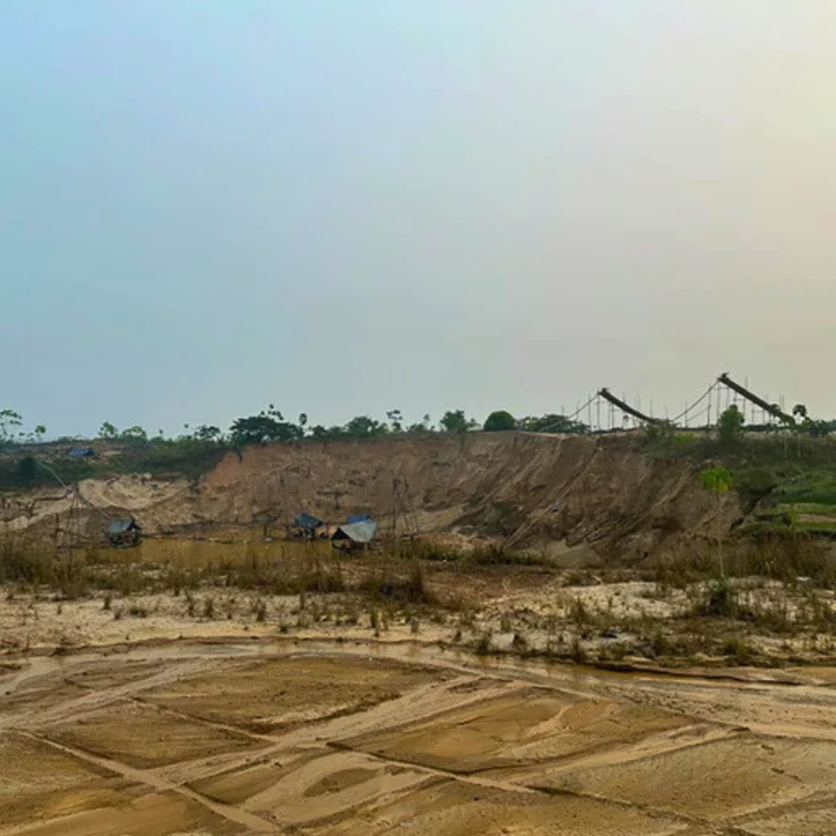 A barren, scarred landscape from suction gold mining in Balata, Peru, showing deep excavated pits, sandy tailings piles, and