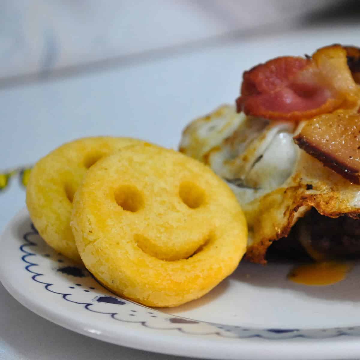 Close up of potato faces next to a far less interesting burger. The faces are made from reformed potato with just two eyes an