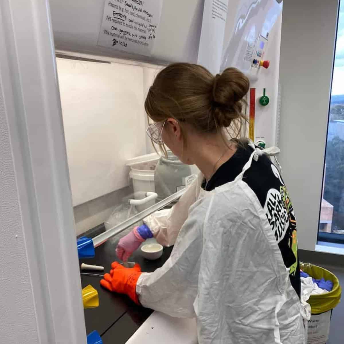 A scientist works on a desk under a fumigated hood. She has her back to camera.